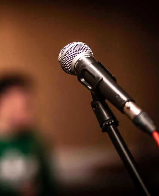 A close-up of a microphone with a blurred drummer in the background. A close-up of a microphone with a blurred drummer in the background.